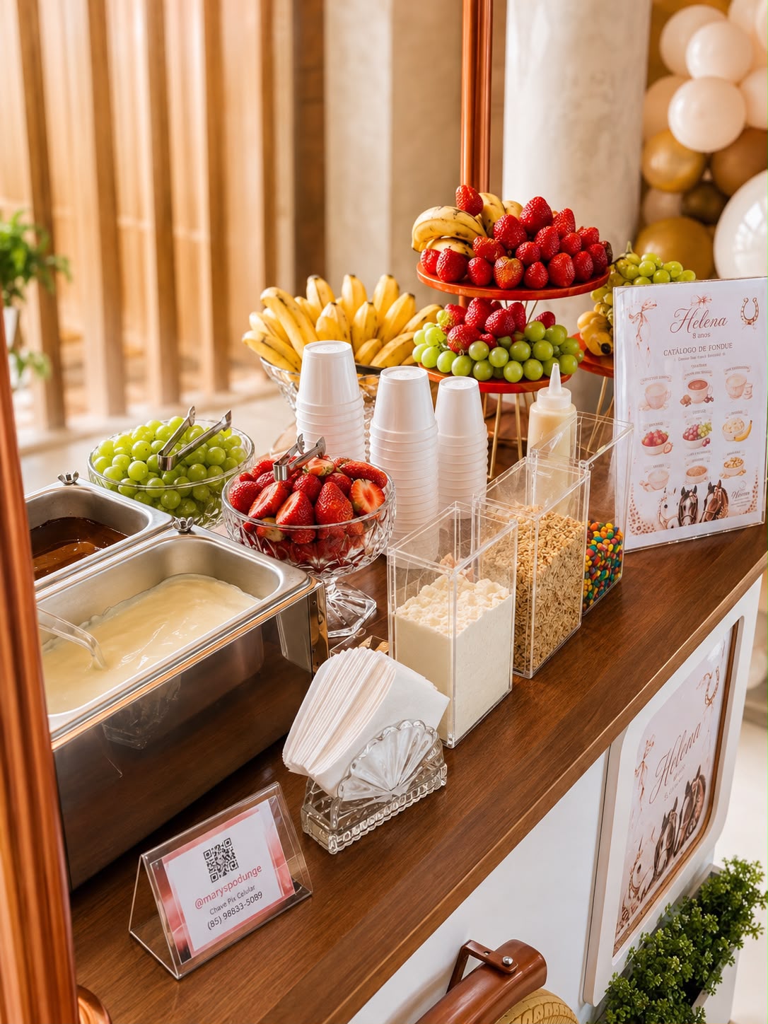 Estação de fondue da Nuvem no Palito com bandejas de chocolate ao leite e branco, morangos, uvas, bananas, complementos em potes e catálogo personalizado do evento