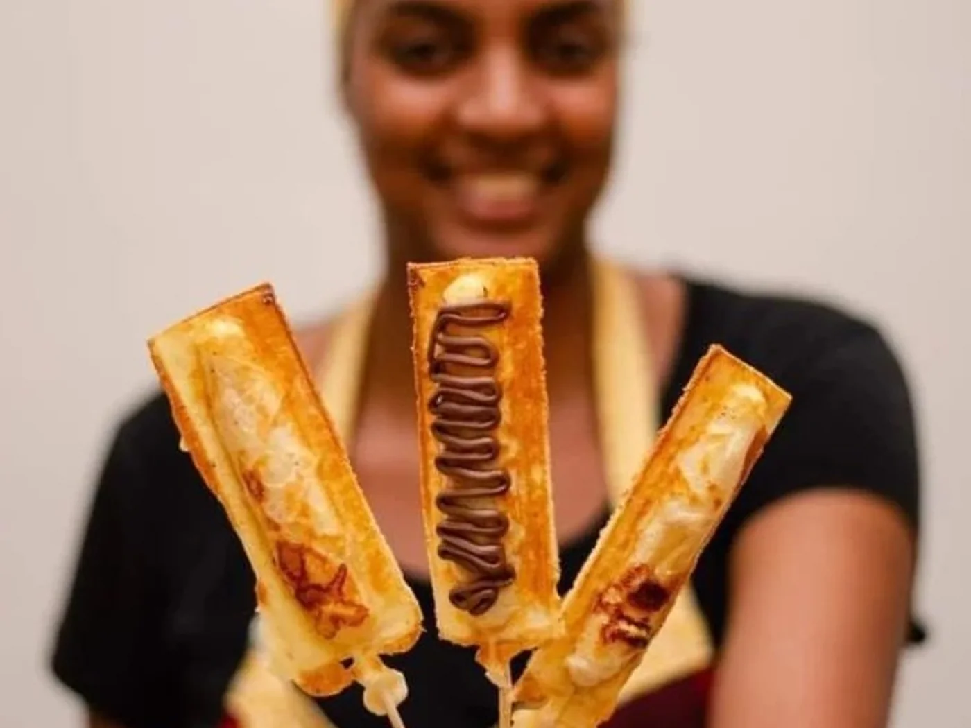 Atendente uniformizada segurando três crepes suíços no palito com cobertura de chocolate
